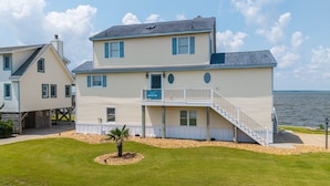 A two-story house with a balcony, a small garden, and a view of the water. - Sunwatch: Soundfront, Hot Tub, Private Boat Dock and Community Pool Access (Nags Head)