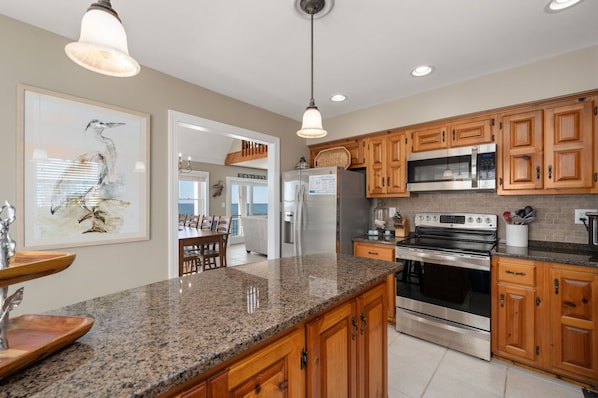 A kitchen with granite countertops, wooden cabinets, stainless steel appliances, and pendant lighting.