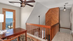 A room with a wooden ceiling fan, a view of the ocean through a door, a wooden staircase, and a carpeted floor. - Sunwatch: Soundfront, Hot Tub, Private Boat Dock and Community Pool Access (Nags Head)