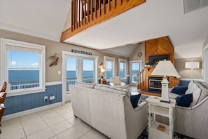 A coastal living room with a view of the sea, a wooden staircase, and a television.