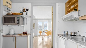 A modern kitchen with white cabinets, a microwave, a coffee maker, and a dining area with yellow chairs. - Awesome apartment in Allinge with WiFi (Allinge)