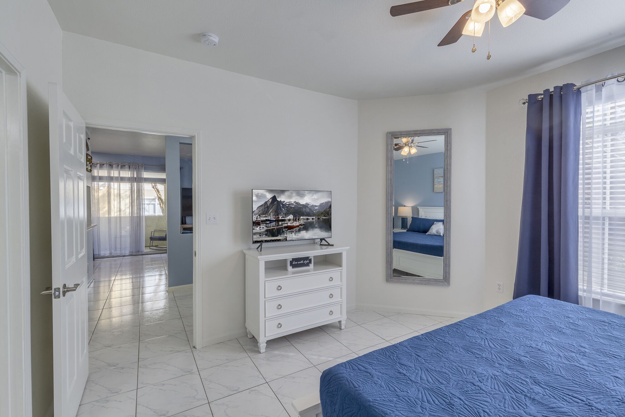 A bedroom with a bed, a dresser, a television, and a large mirror.