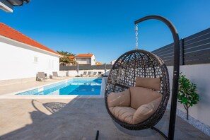 Relax in a serene outdoor setting with a hanging chair and pool.