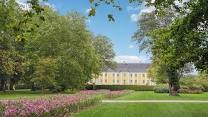 A large, yellow building with a symmetrical facade, surrounded by lush greenery and flowering plants. - Gorgeous home in Næstved (Næstved)