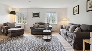 A living room with two sofas, a coffee table, and two lamps. There are two windows with white frames and a framed picture on the wall. - Gorgeous home in Næstved (Næstved)