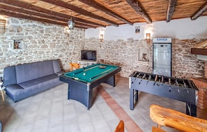 A room with a pool table, sofa, and foosball table, with stone walls and wooden beams.