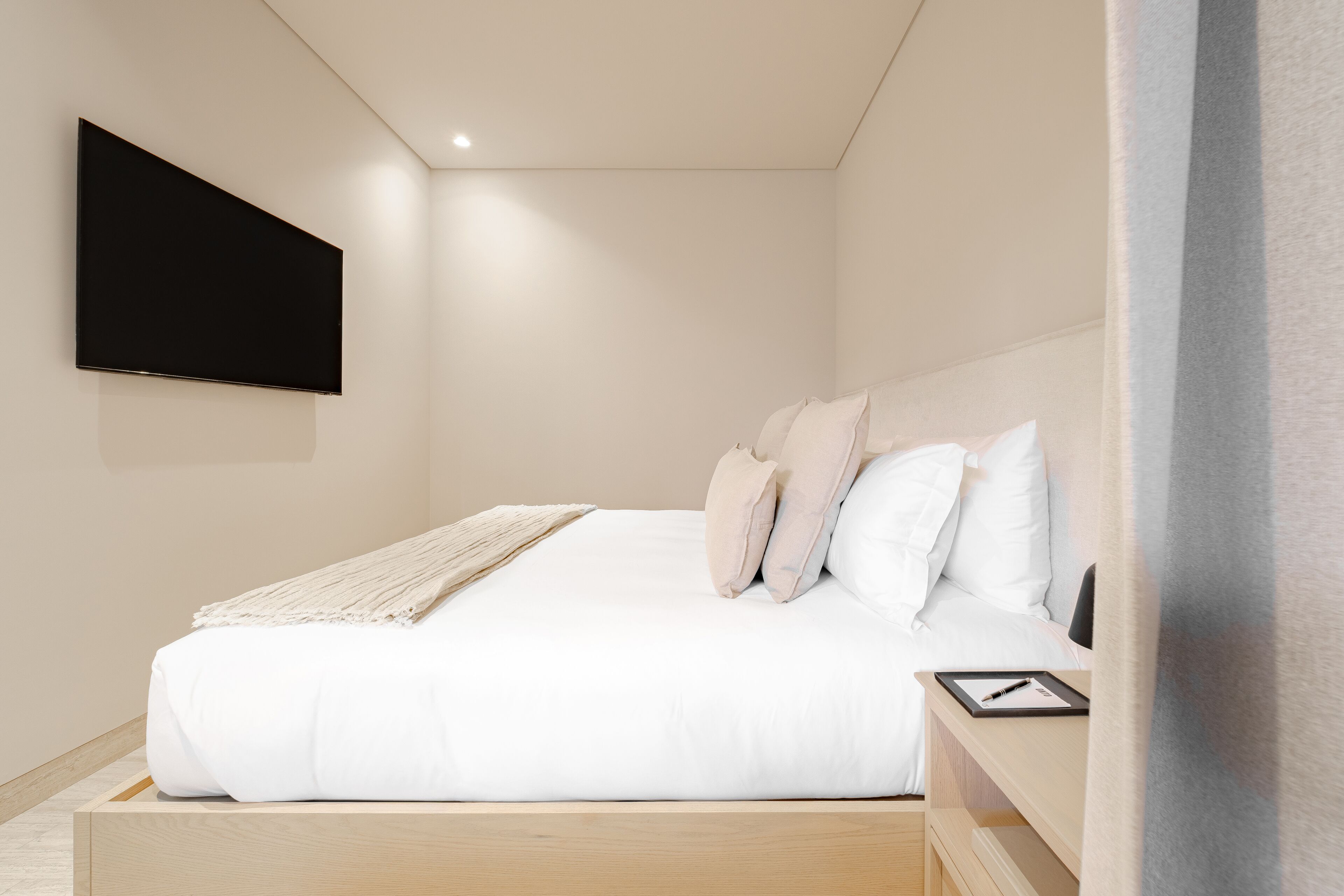 Une chambre à coucher moderne avec un lit, une table de chevet, un téléviseur à écran plat fixé au mur et une tête de lit en bois.