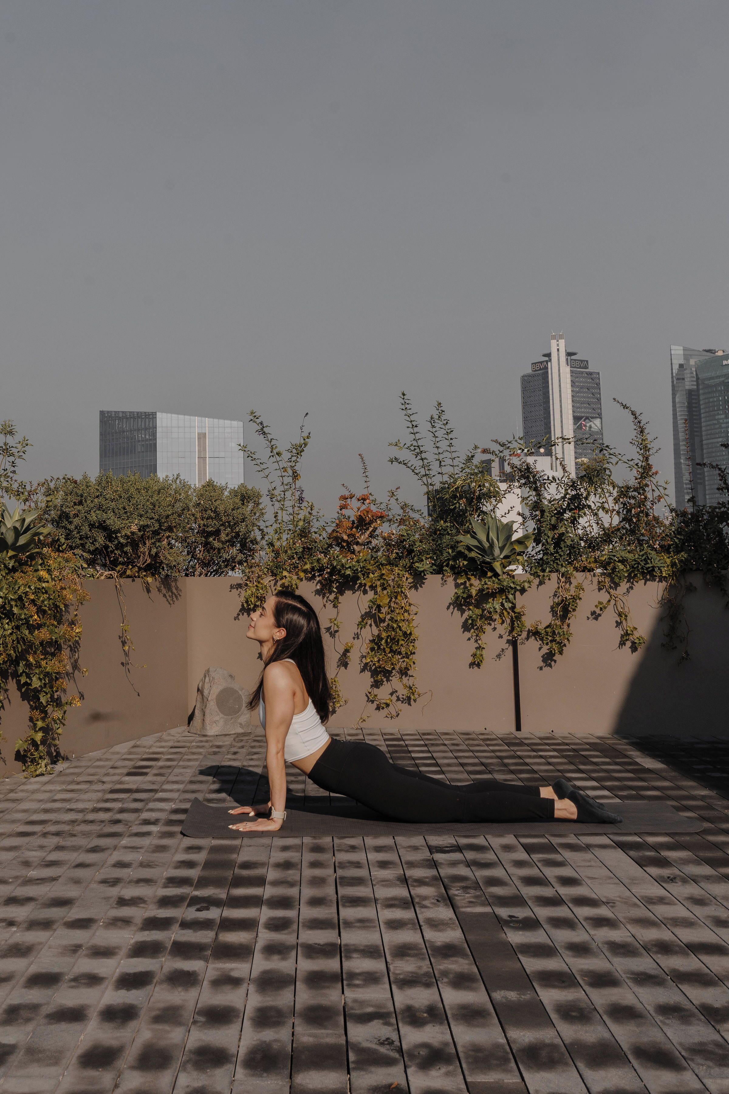 Una persona realizando una postura de yoga en una azotea con un paisaje urbano de fondo.
