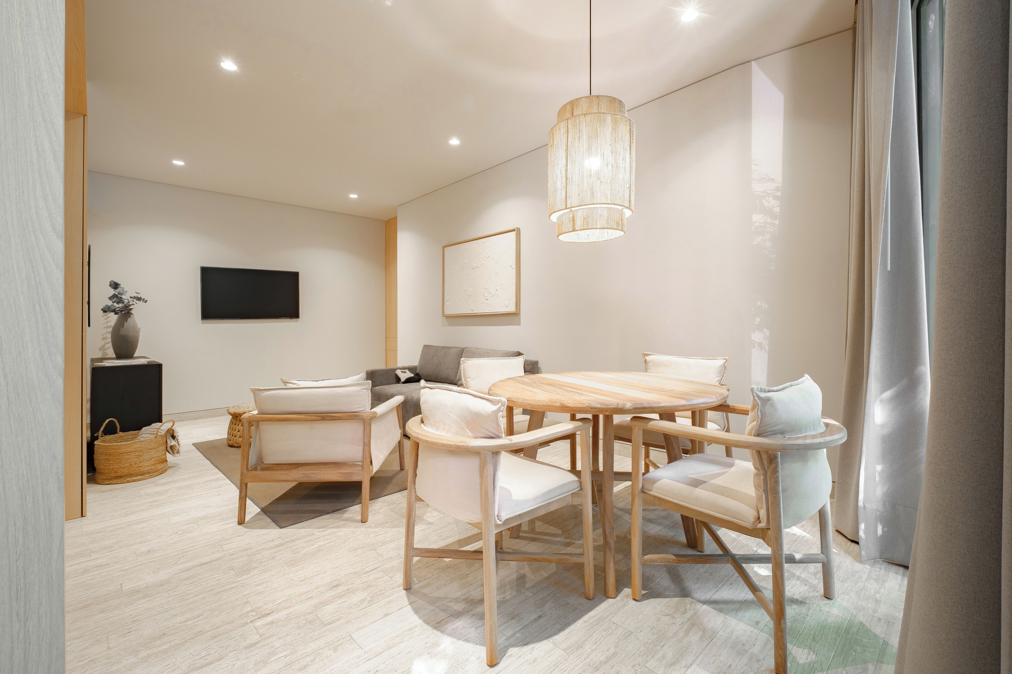 A modern dining area with a wooden table and chairs, a hanging light fixture, and a flat-screen TV on the wall.