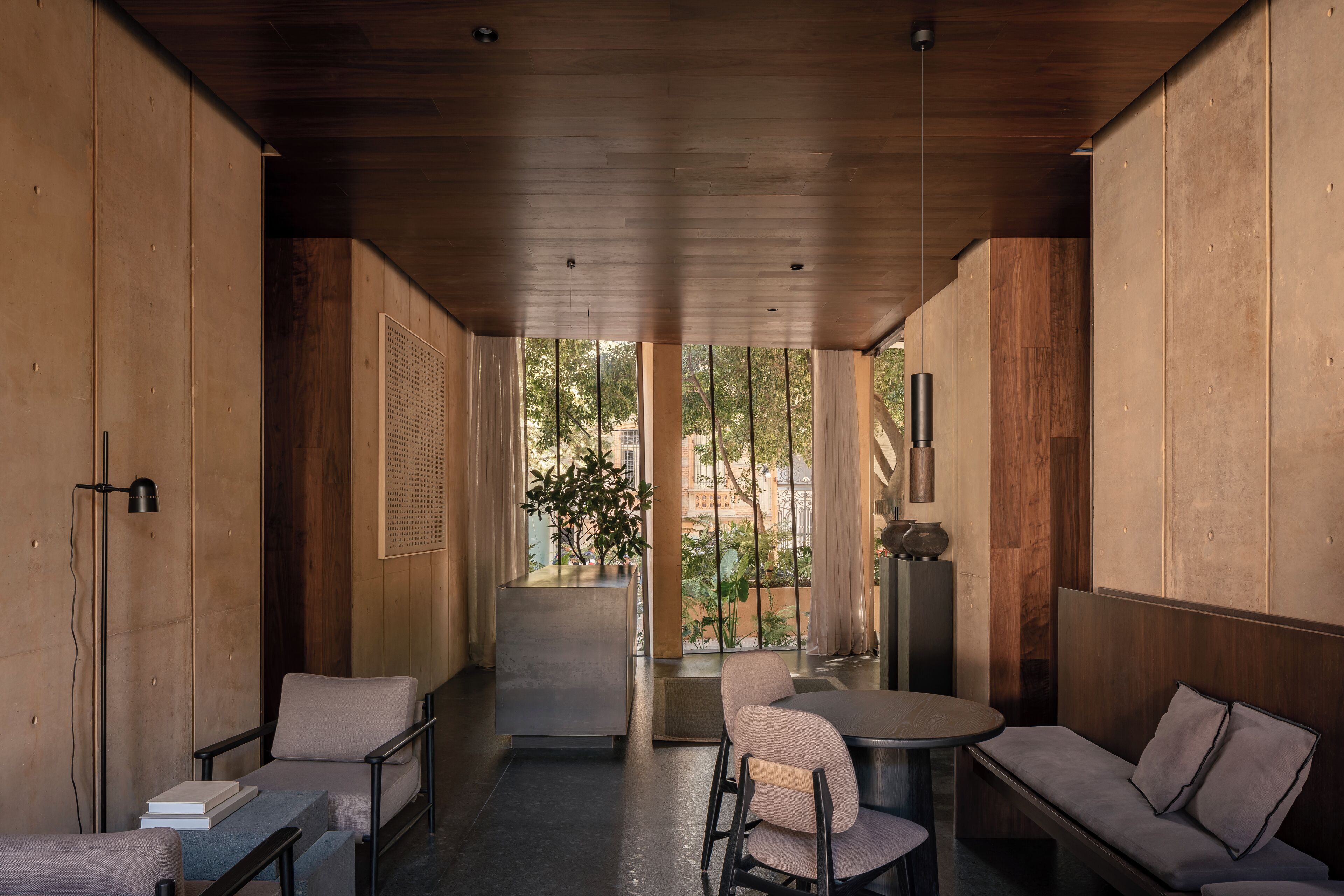 A modern interior with a wooden ceiling, a dining area with a round table and chairs, a sofa, and a small bookshelf.