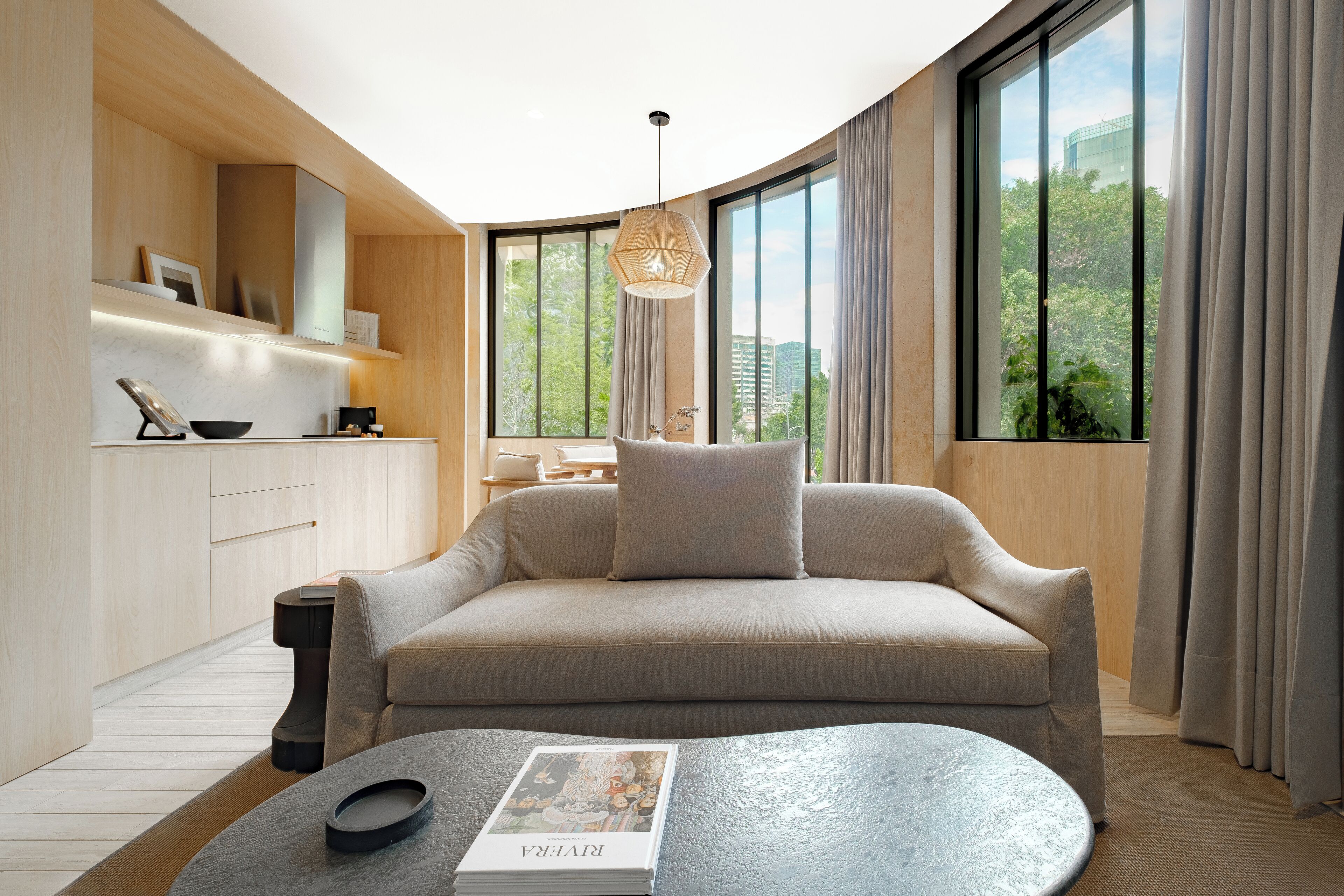 A modern living room with a sofa, a coffee table, and a view of greenery through large windows.