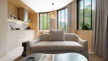 A modern living room with a sofa, a coffee table, and a view of greenery through large windows.