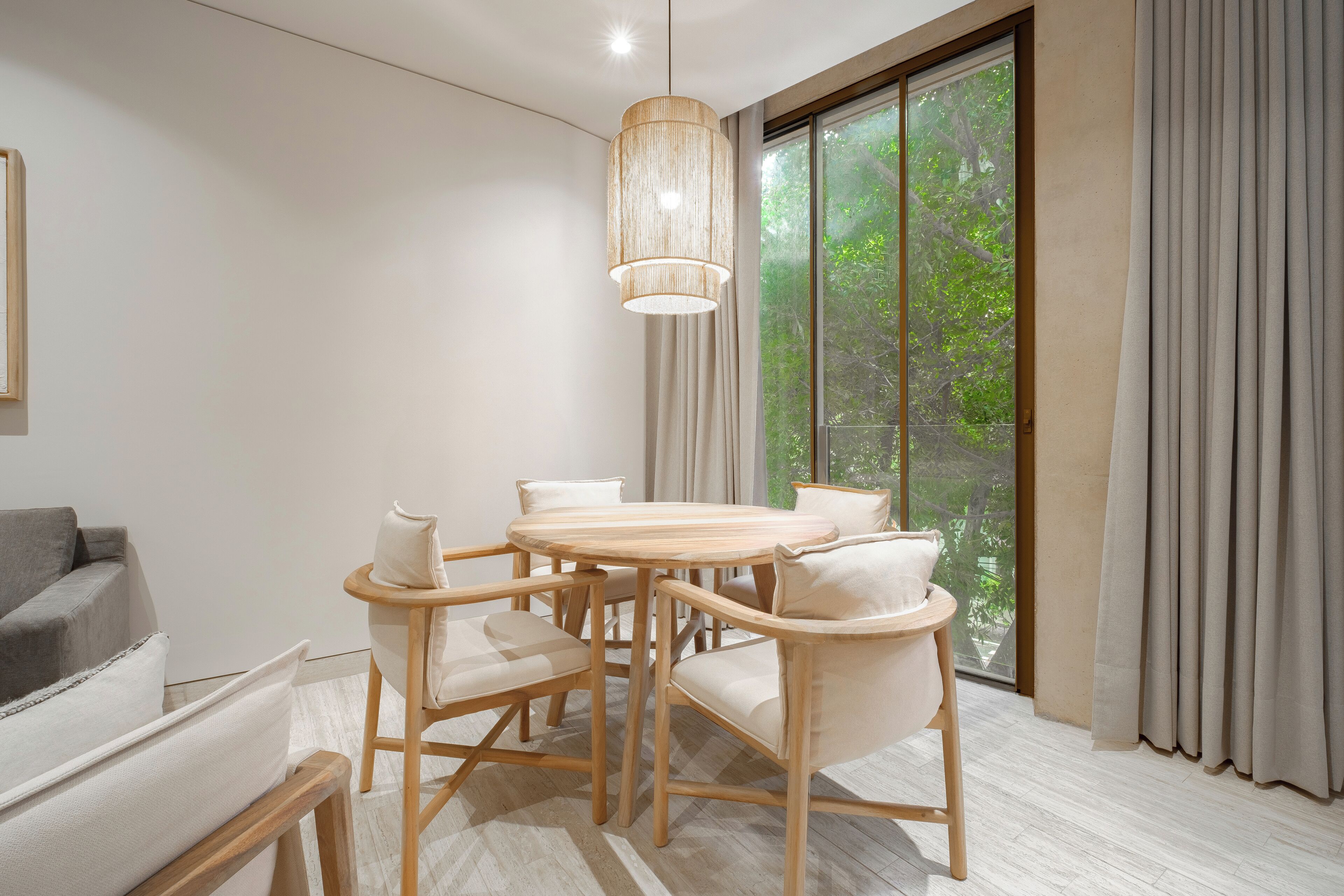 Zona pranzo moderna con tavolo rotondo e sei sedie, lampadario a sospensione e un'ampia finestra con tende.