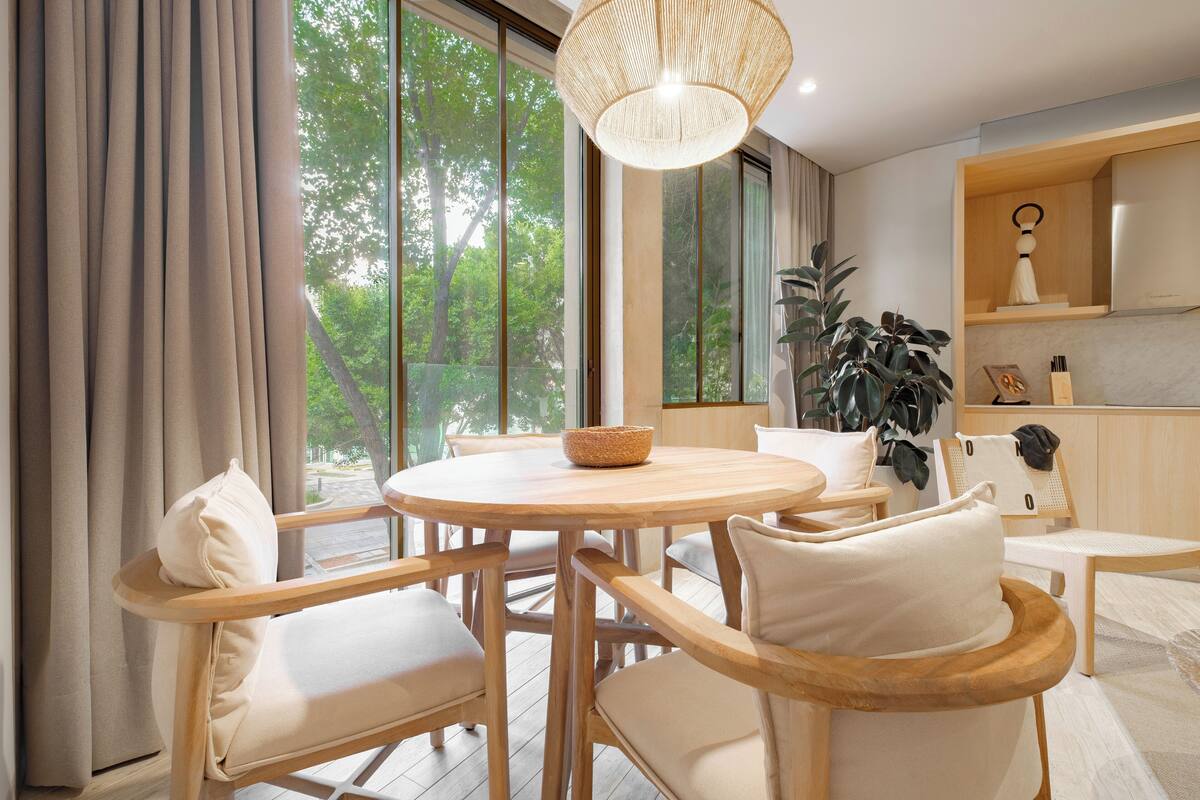 Un comedor moderno con una mesa redonda de madera, sillas acolchadas y una lámpara colgante.
