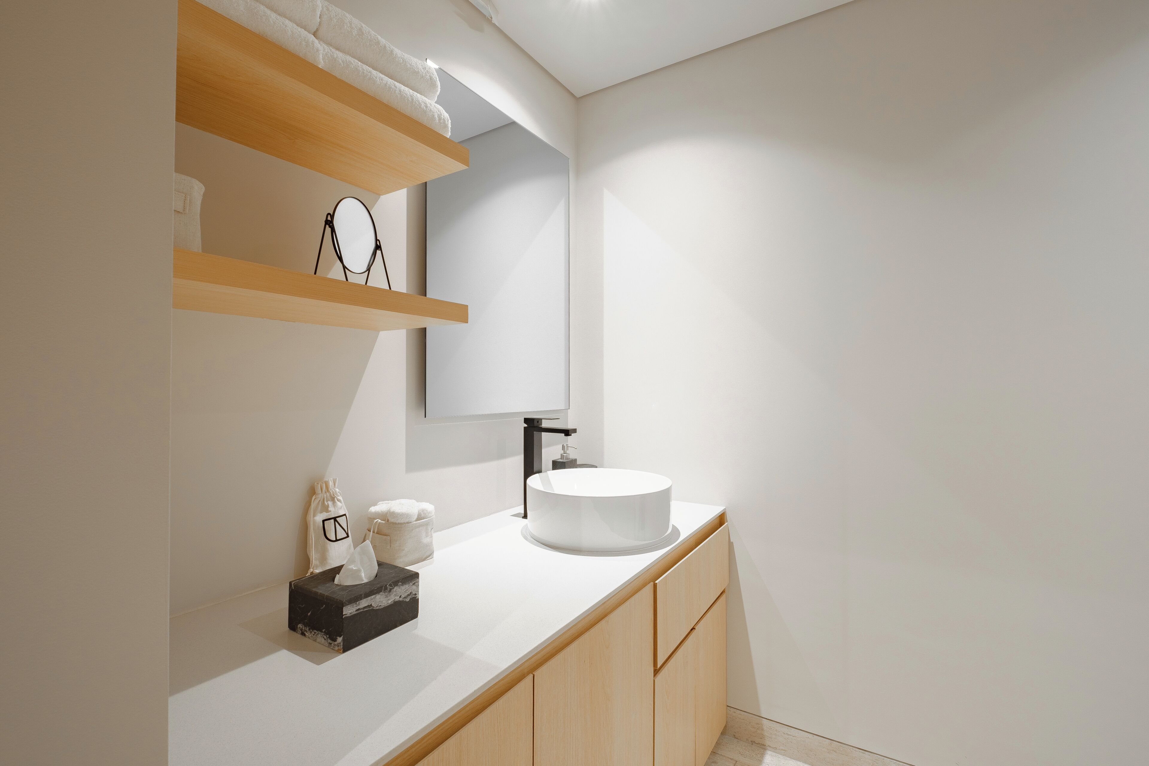 A modern bathroom with a round sink, wooden shelves, a mirror, and a towel rack.