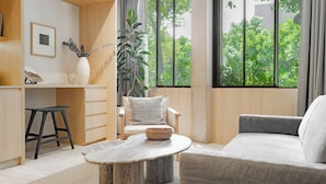 A modern living room with a sofa, a round wooden table, a chair, and a large window with a view of greenery. - ONTO Tonalá Mexico City (Mexico City)