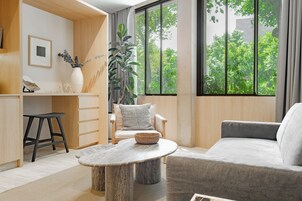 Un salon moderne avec un canapé, une table ronde en bois, un fauteuil et une grande fenêtre donnant sur un paysage verdoyant.