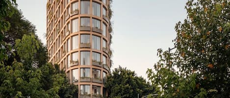 A modern, multi-story building with a curved facade, surrounded by lush greenery and a pedestrian walkway.
