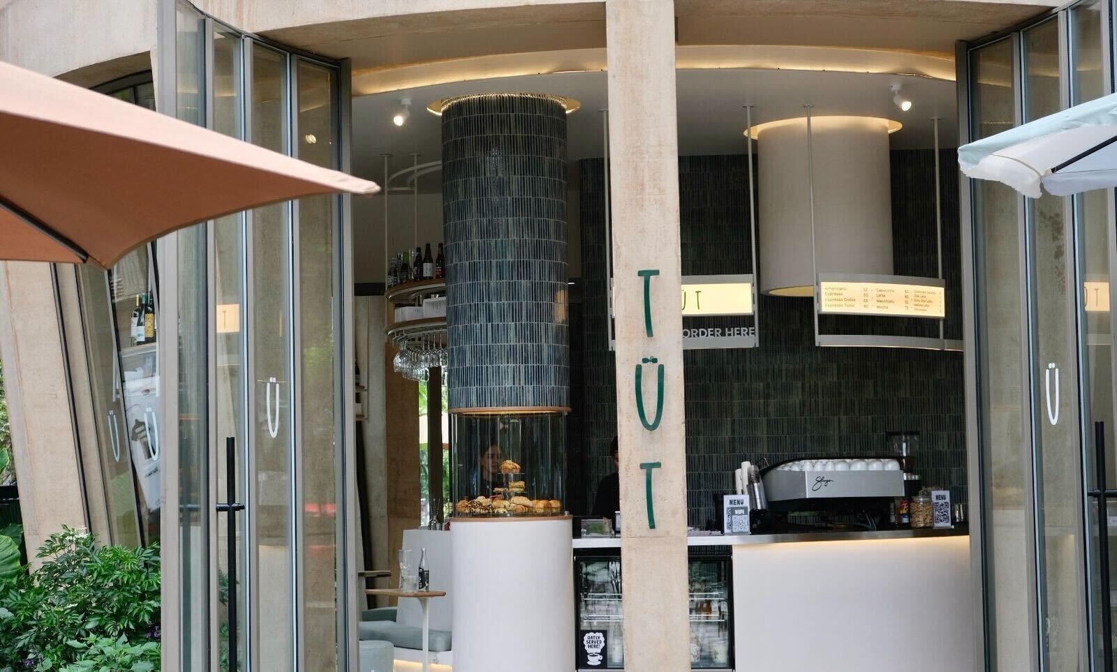 A modern bar area with a glass enclosure, a menu board, and a counter with a coffee machine.