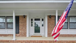 Une maison à deux étages avec un porche à l’avant, une façade en briques et un drapeau.