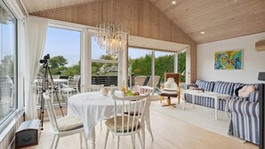 A spacious room with a large window, a dining area with a table and chairs, a sofa, and a painting on the wall.