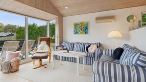 A spacious living area with a large window, a striped sofa set, a white coffee table, and a wicker chair.