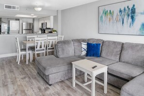 A modern living room with a grey sectional sofa, a small white table, and a dining area with white chairs.