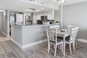 A modern kitchen with white cabinetry, a central island, and a dining area with white chairs.