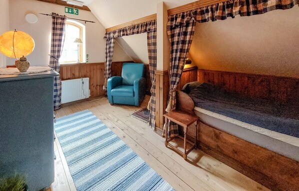 Una habitación acogedora con un sofá azul, una silla de madera, un ventanal con cortinas a cuadros y un radiador.