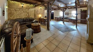Un interior rústico con pared de piedra, sofá de cuero, un barril de madera y un comedor con muebles de madera.