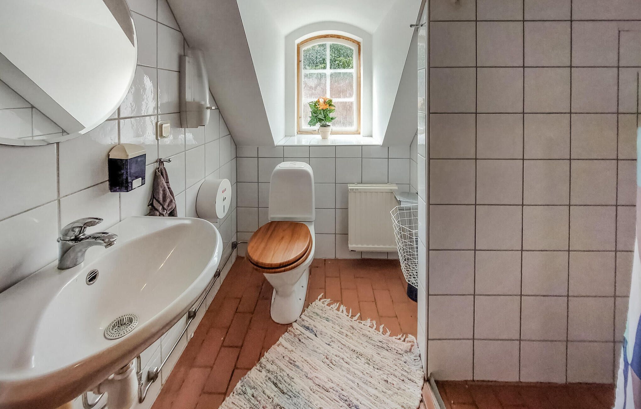 A bathroom with a white sink, a wooden toilet, a white radiator, and a window with a plant.