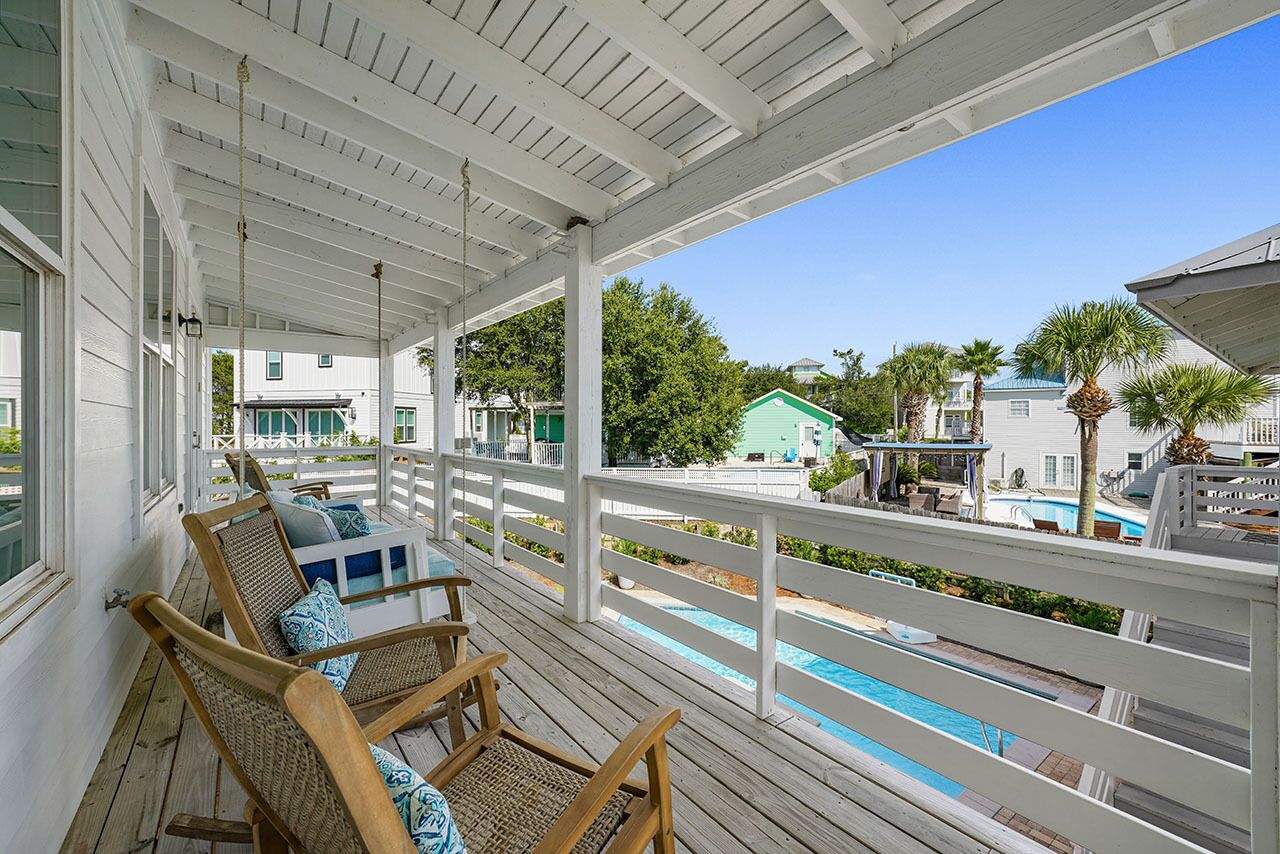 A wooden deck with wicker chairs and a pool in the background.