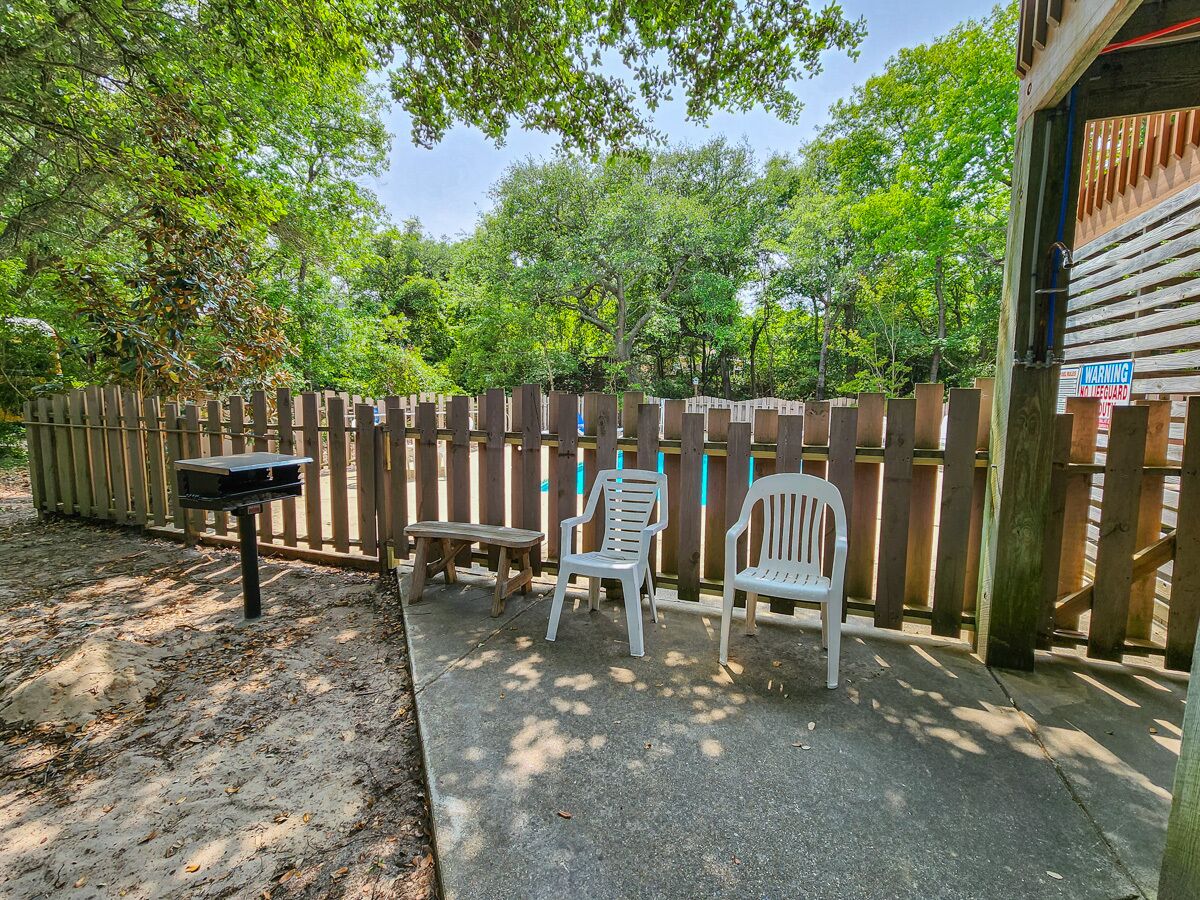 A fenced outdoor area with a bench, two white chairs, and a mailbox.