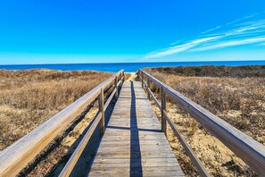 Une promenade en bois menant à la plage, avec des dunes de sable et un ciel bleu dégagé.