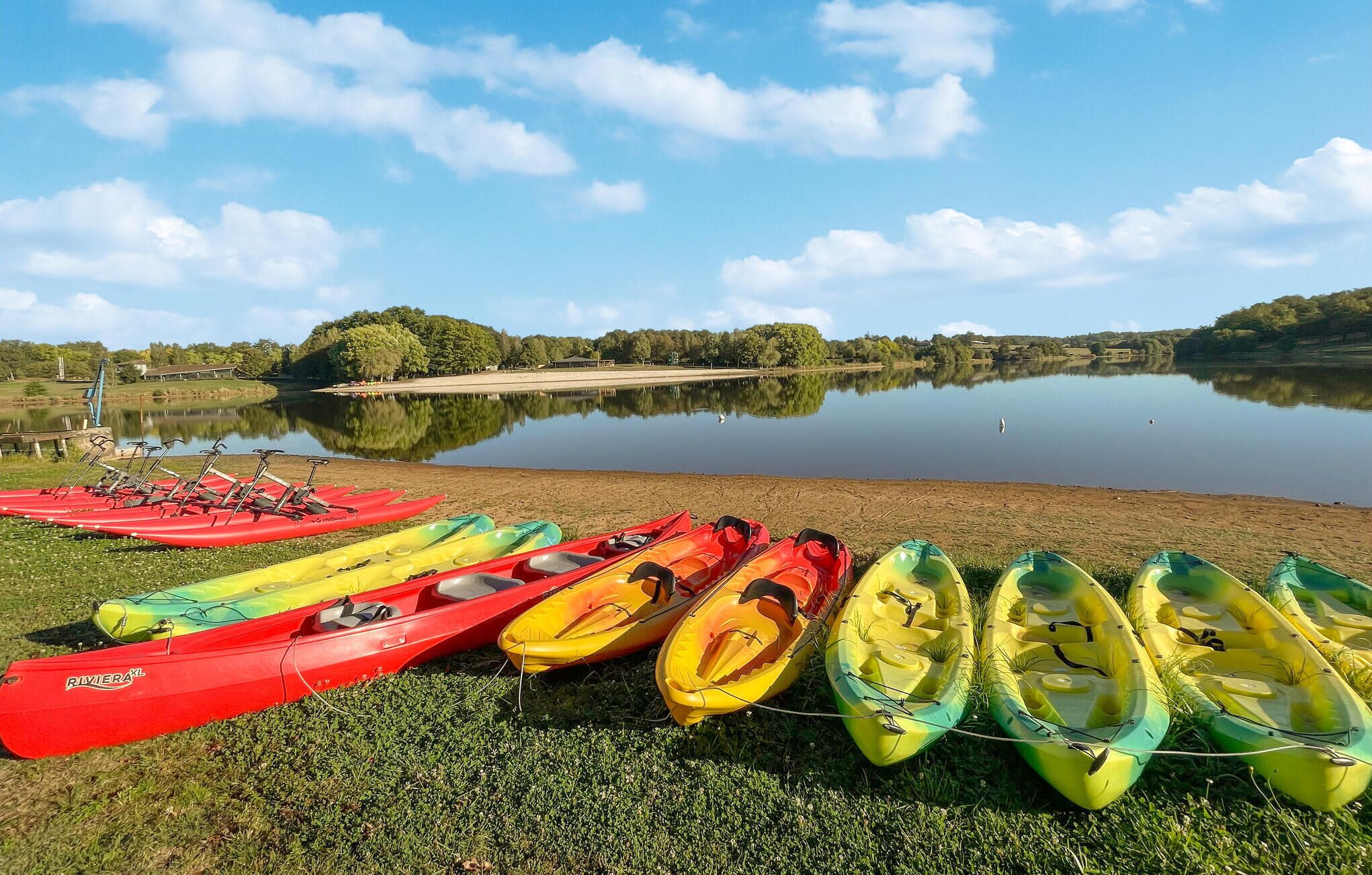 A lakeside view with several kayaks lined up on the shore.