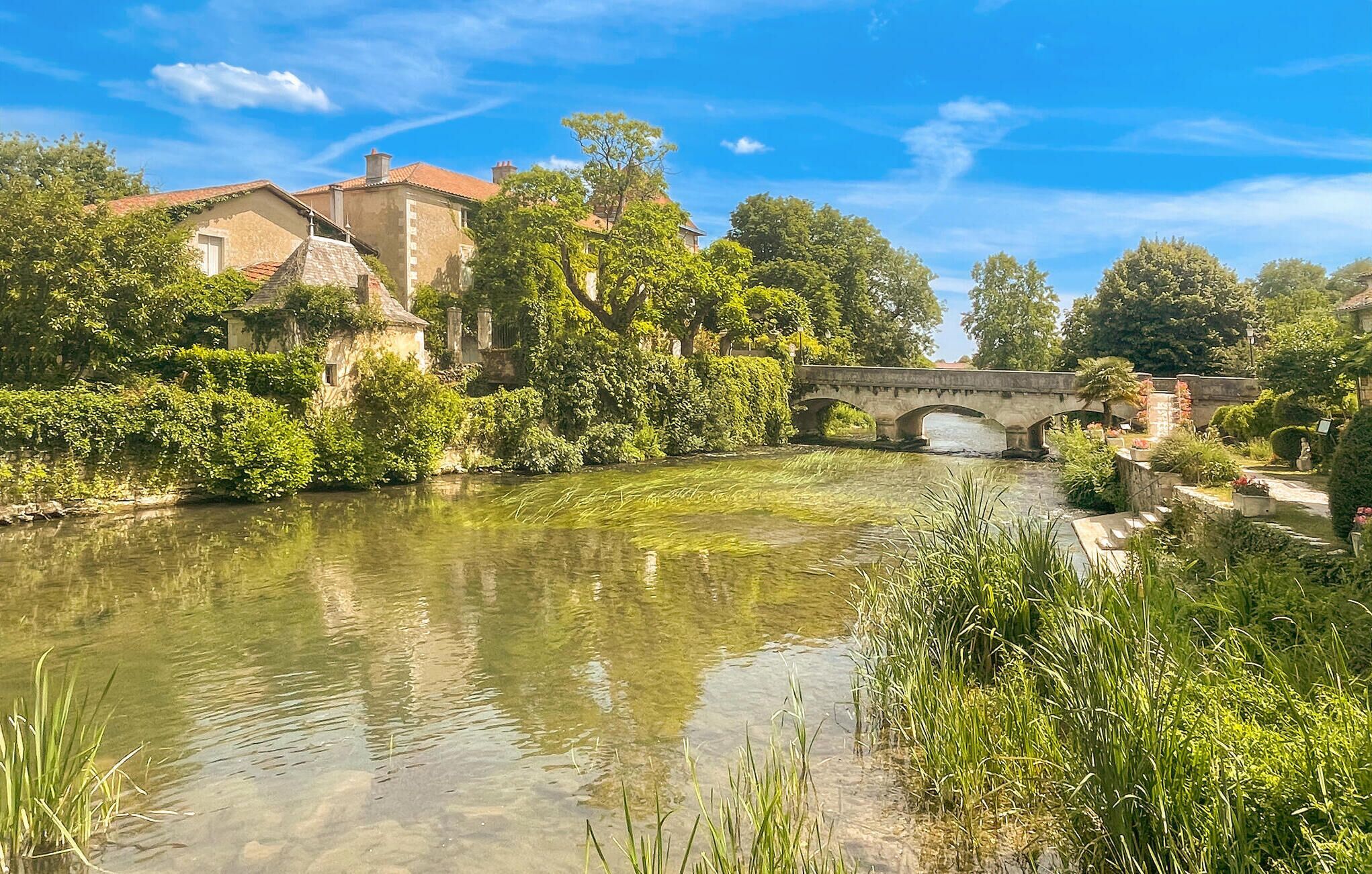 Ein Fluss mit einer Steinkonstruktion, umgeben von üppiger Vegetation und historischen Gebäuden.