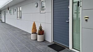 A modern building with a grey facade, a dark blue door, and two potted plants.