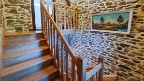 Un escalier en bois, un mur en pierre et un tableau représentant un paysage.