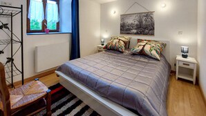 Une chambre à coucher comprenant un lit, une chaise, une fenêtre avec des rideaux, un tableau accroché au mur et des lampes de chevet.