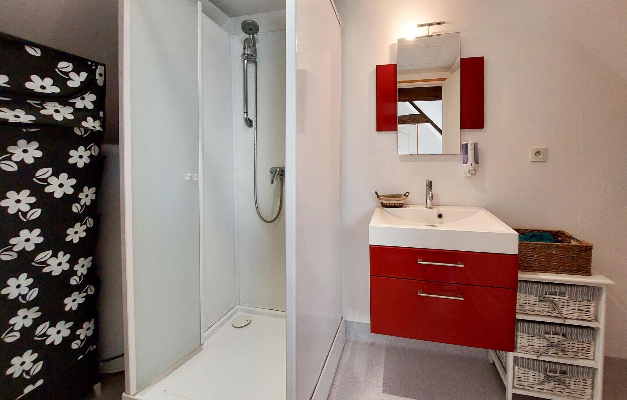 A bathroom with a shower, a sink, a mirror, and a red cabinet.