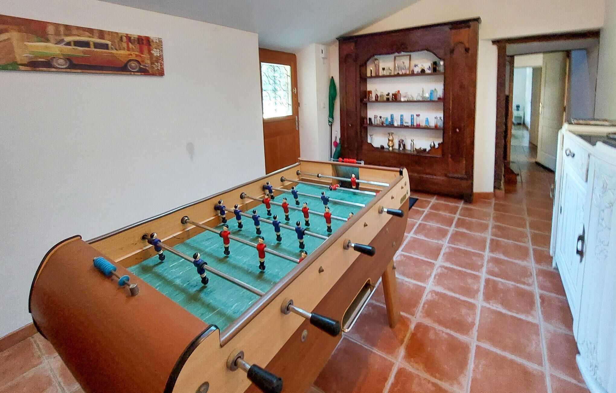 A foosball table in a room with tiled flooring and a wooden cabinet with glassware.
