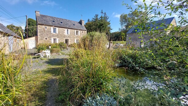 Un bâtiment en pierre avec un toit en pente, un chemin de gravier et un petit étang.
