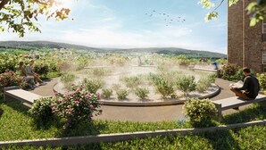 Un jardín ajardinado con un área circular central, bancos y un edificio de piedra al fondo.