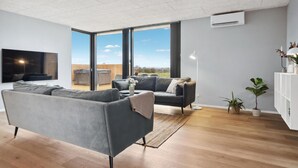A modern living room with a grey sofa, a black armchair, a flat-screen TV, and a large window offering a view of the outdoors. - Amazing home in Børkop with sauna (Børkop)