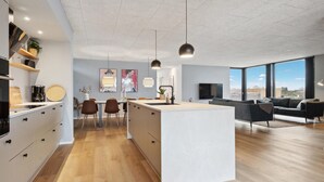 A modern kitchen with a central island, dining area with chairs, and a living space with a sofa and large windows. - Amazing home in Børkop with sauna (Børkop)