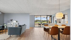 A modern living room with a grey sofa, a dining area with wooden chairs, and a kitchen with pendant lights. - Amazing home in Børkop with sauna (Børkop)