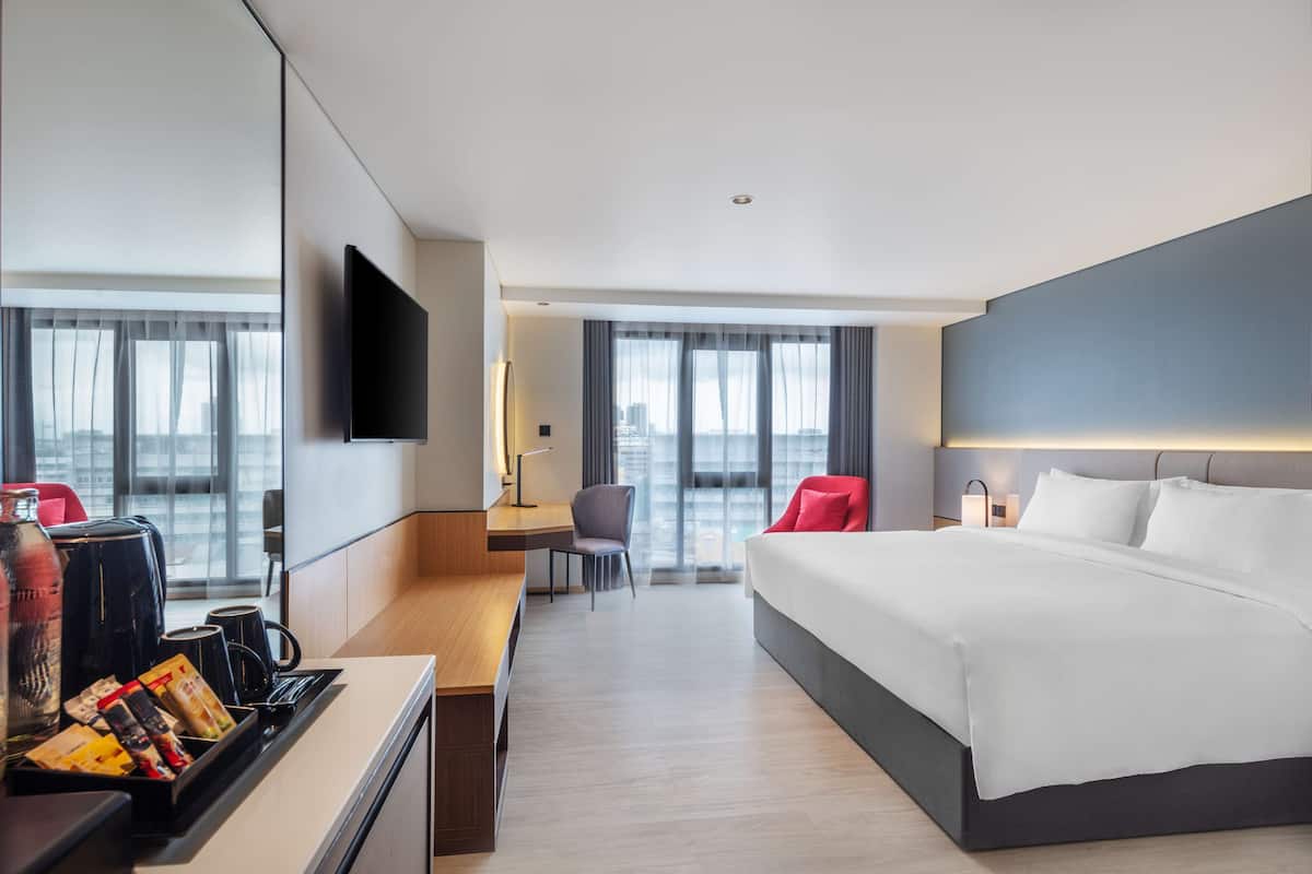 Ein modernes Hotelzimmer mit einem großen Bett, einem Schreibtisch mit Stuhl, einem Flachbildfernseher und Blick auf die Stadt durch große Fenster.
