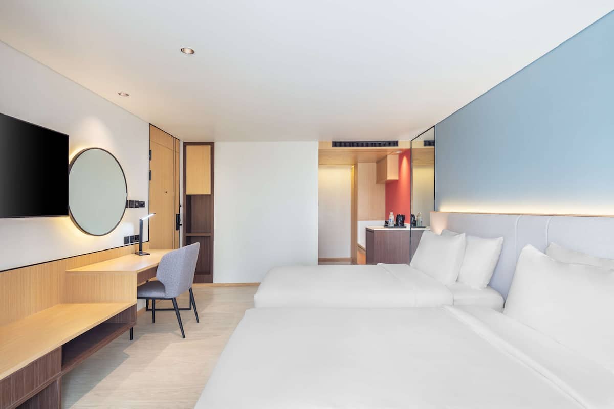Ein modernes Hotelzimmer mit einem großen Bett, einem Schreibtisch, einem Sessel, einem runden Spiegel und einem Fernseher.