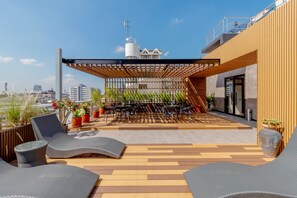 Terraço no telhado com espreguiçadeiras, área de refeições e plantas em vasos.