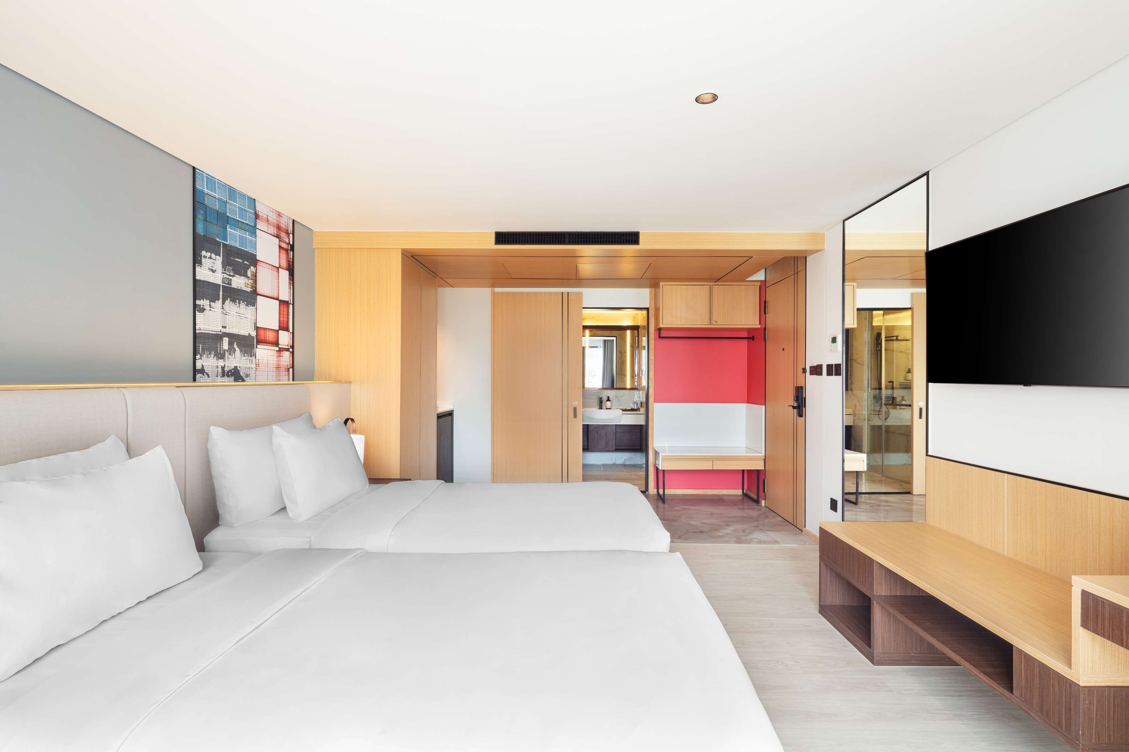 A modern hotel room with a large bed, a TV, and a kitchenette in the background.